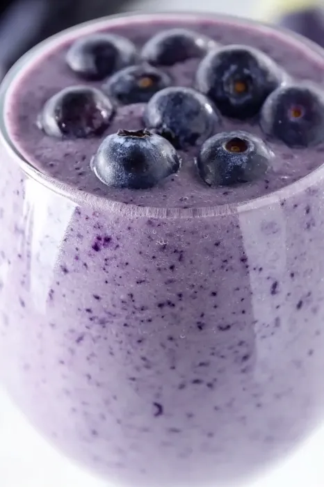 A glass of blueberry smoothie with blueberries in it.