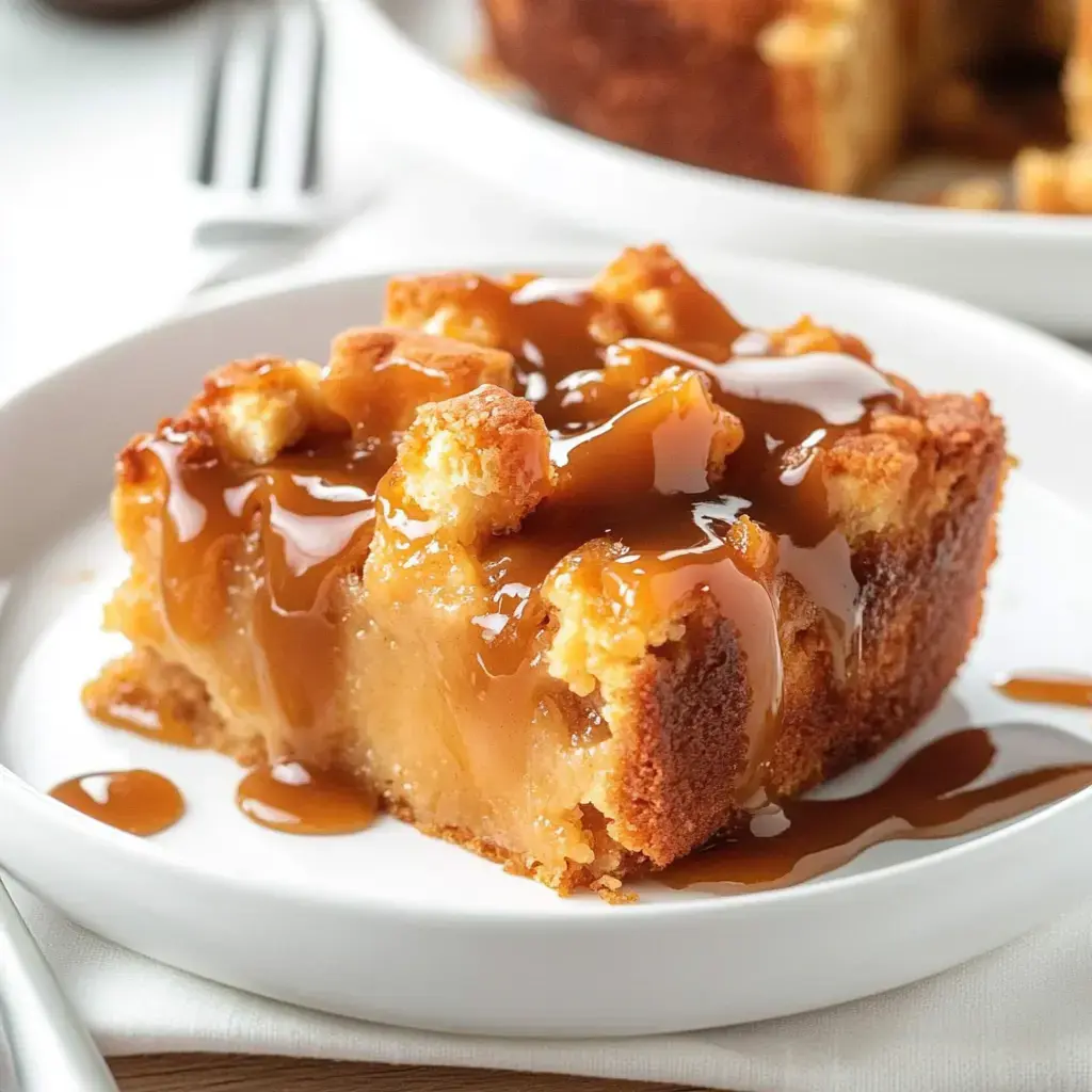 A slice of caramel apple cake drizzled with caramel sauce on a white plate.