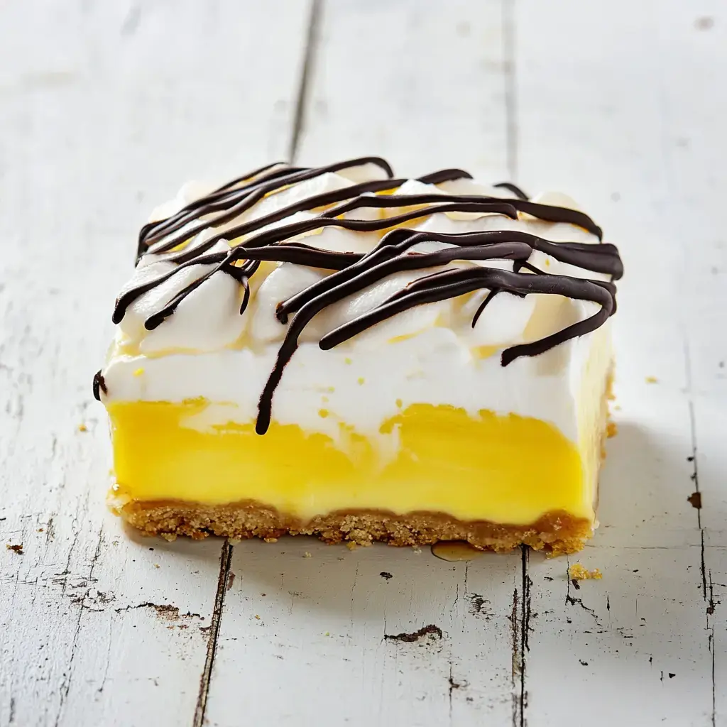 A slice of yellow dessert with a creamy layer, topped with whipped cream and drizzled chocolate, sits on a rustic white wooden surface.