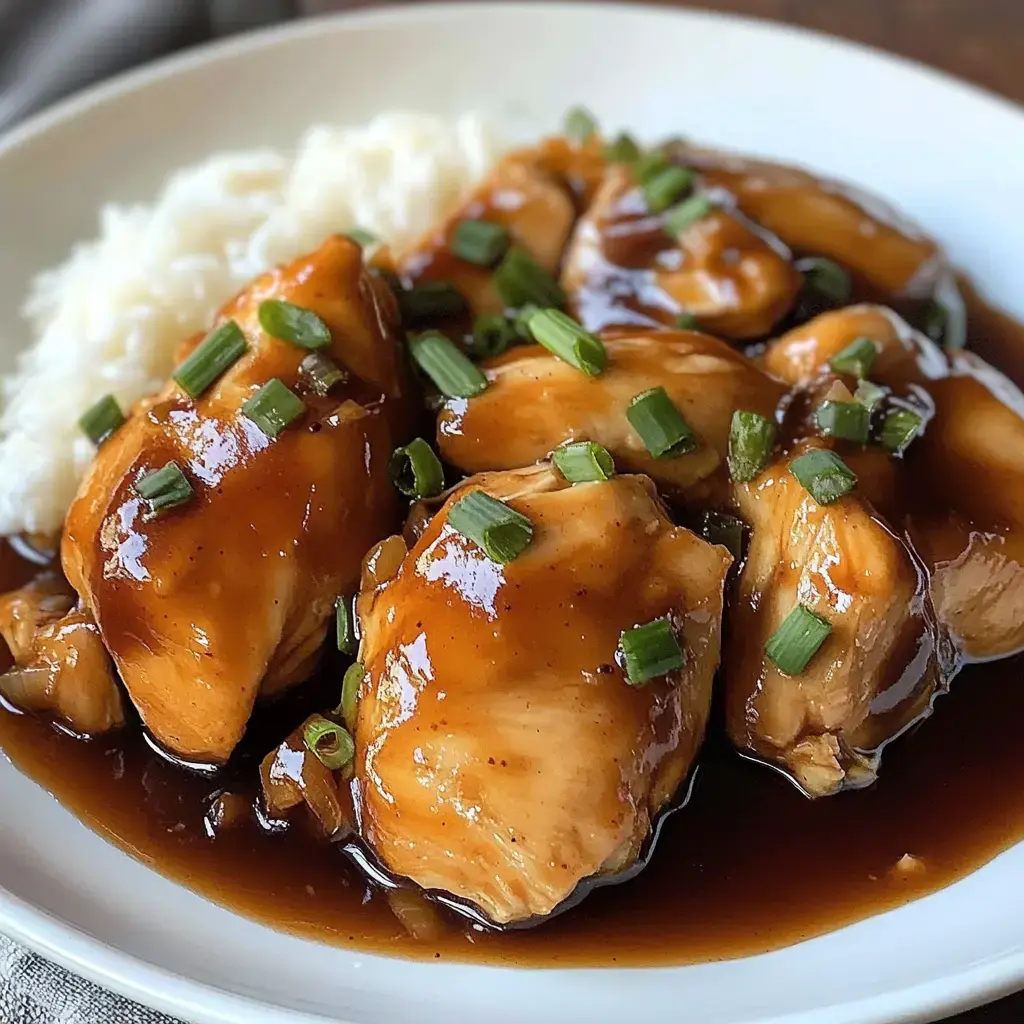 A plate of tender chicken pieces glazed with a savory sauce, garnished with green onions, served alongside fluffy white rice.