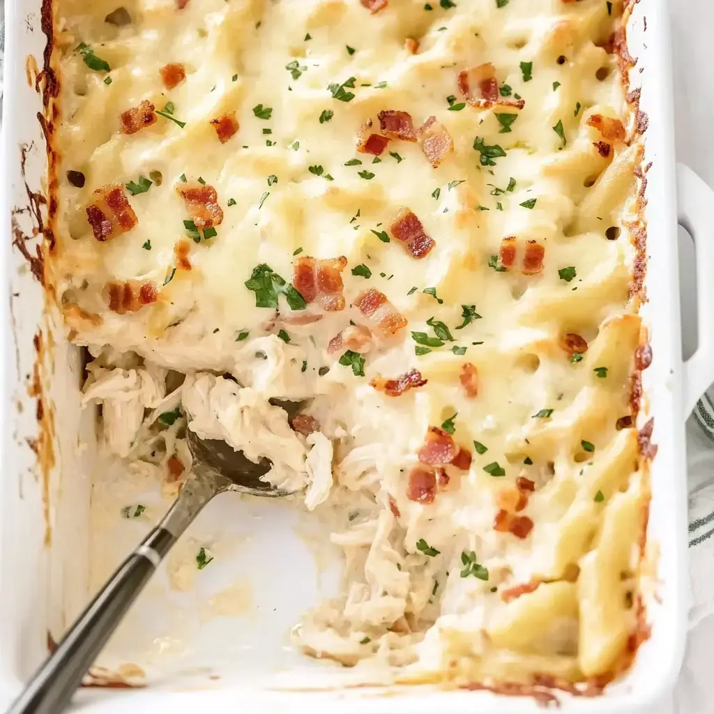 A baked pasta dish with creamy sauce, shredded chicken, and bacon bits, garnished with chopped parsley.