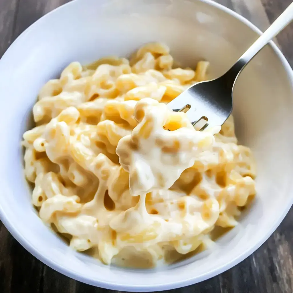 A bowl of creamy macaroni and cheese with a fork lifting a portion from the dish.