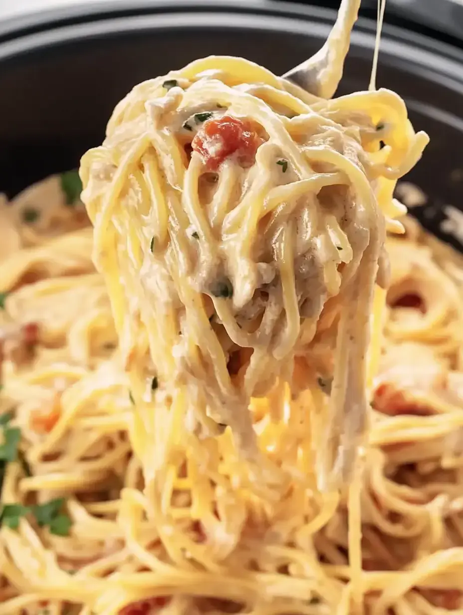 A fork holding creamy spaghetti with herbs and small pieces of meat, lifted from a bowl of pasta.