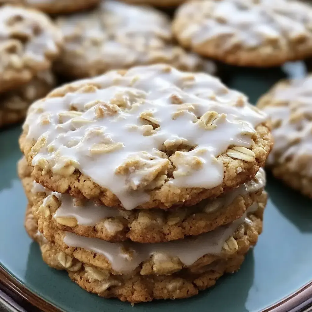 Three stacked oatmeal cookies with a white icing glaze, surrounded by more cookies on a plate.