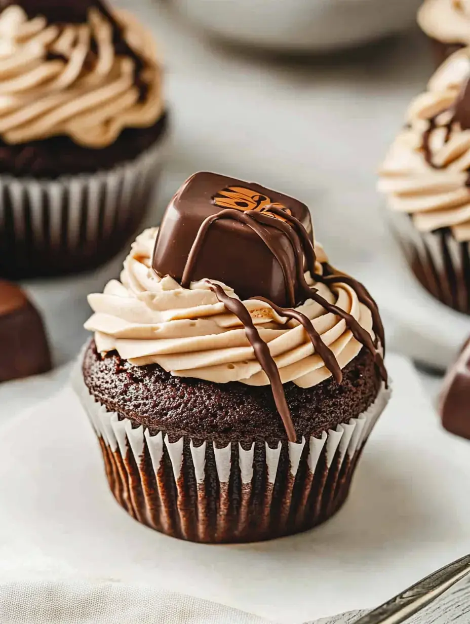 A chocolate cupcake topped with swirls of peanut butter frosting and a chocolate confection sits on a light surface.