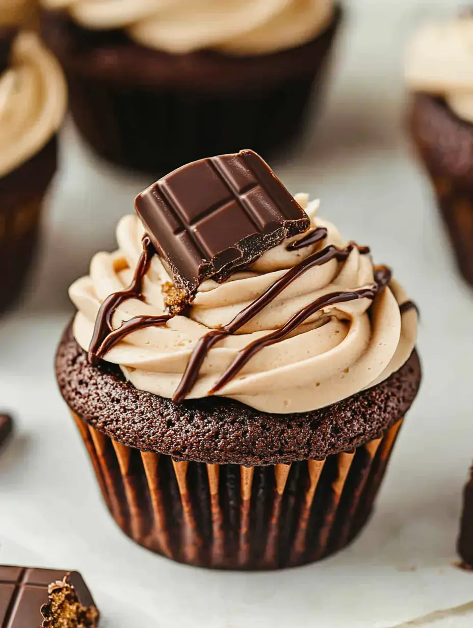 A chocolate cupcake topped with creamy frosting, drizzled with chocolate, and featuring a piece of chocolate on top.