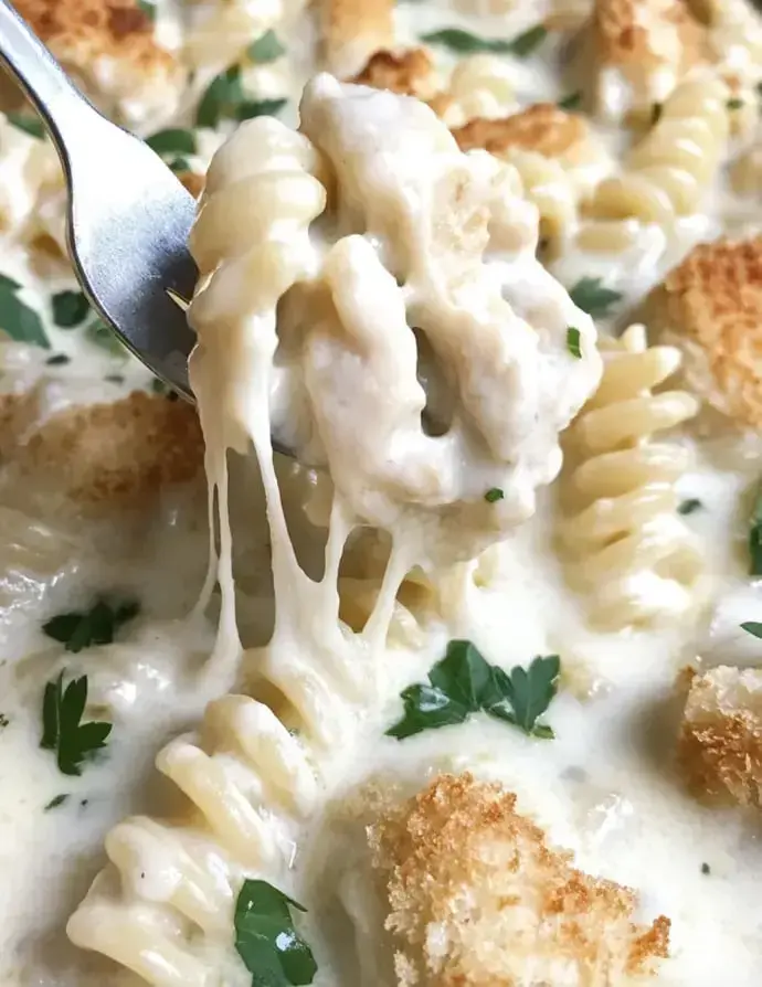 A fork holding creamy, cheesy pasta with melted cheese and breadcrumbs, surrounded by parsley.