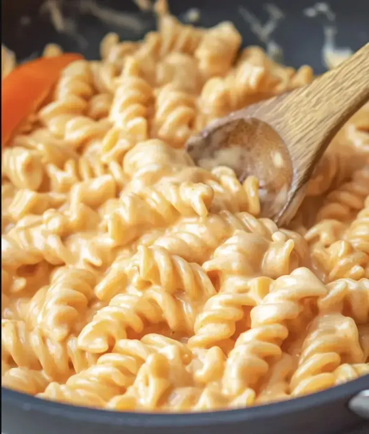 A pot of creamy macaroni and cheese with rotini pasta, stirred with a wooden spoon.