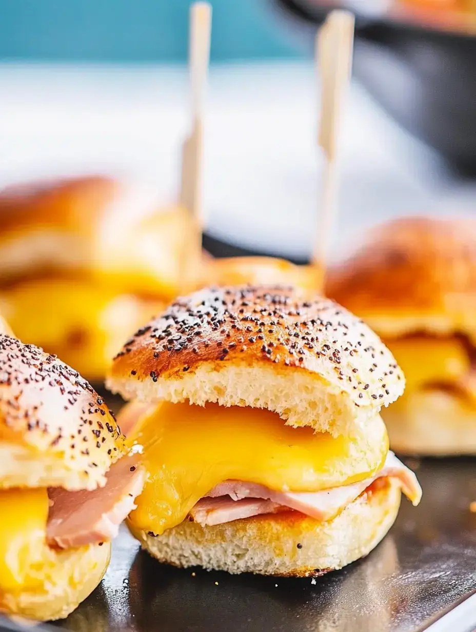 A close-up of savory sliders filled with layers of cheddar cheese and ham, topped with poppy seeds on a toasted bun.