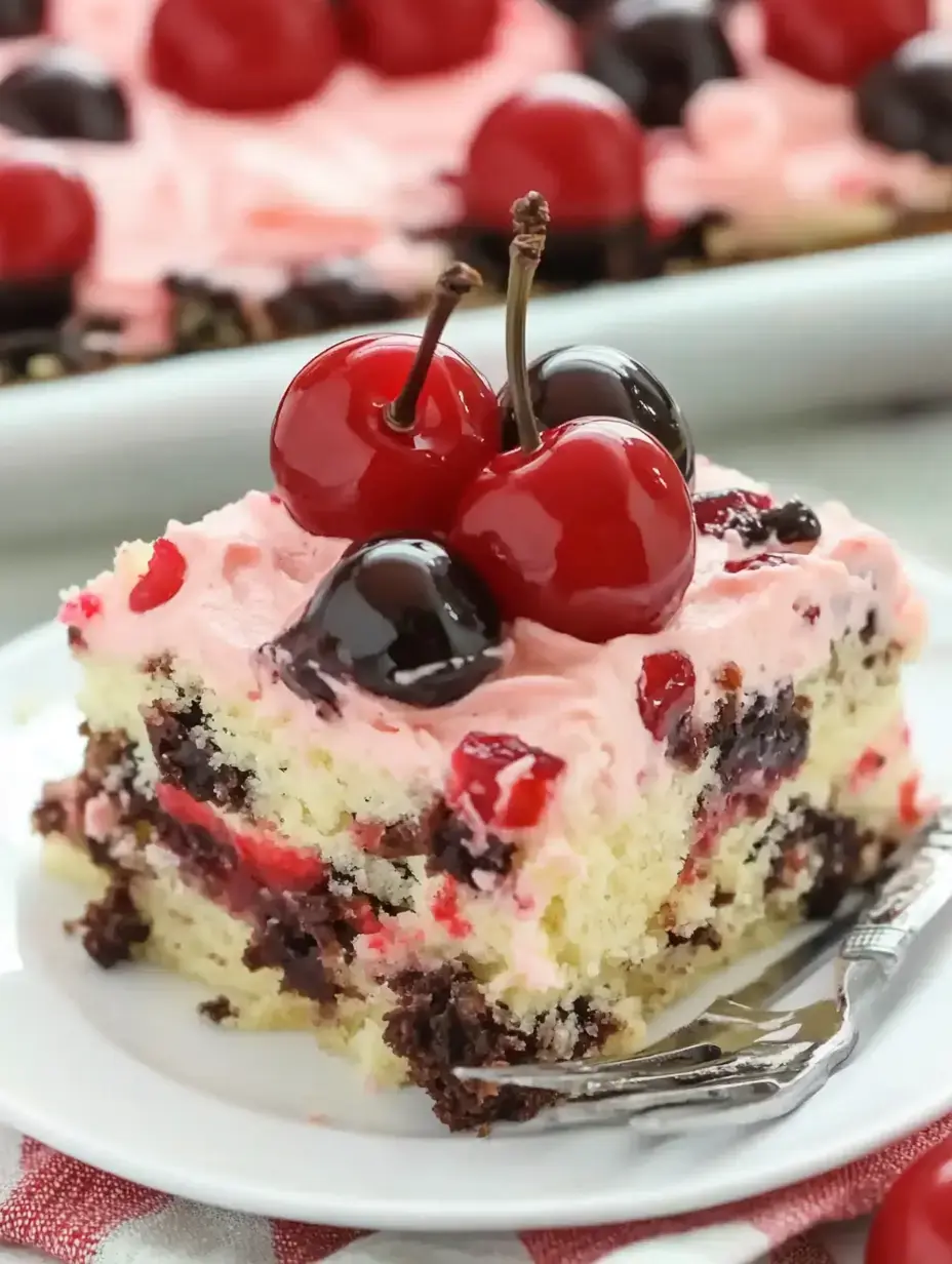 A slice of colorful cake topped with pink frosting and red and black cherries, served on a white plate.