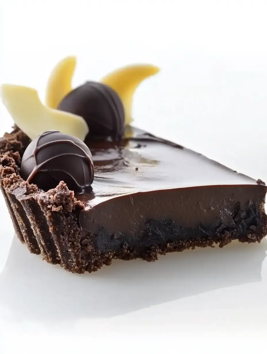 A slice of chocolate tart with a glossy ganache topping, decorated with dark chocolate truffles and white chocolate curls.