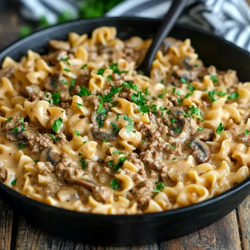 A close-up view of creamy beef and mushroom pasta, garnished with fresh parsley in a black bowl.