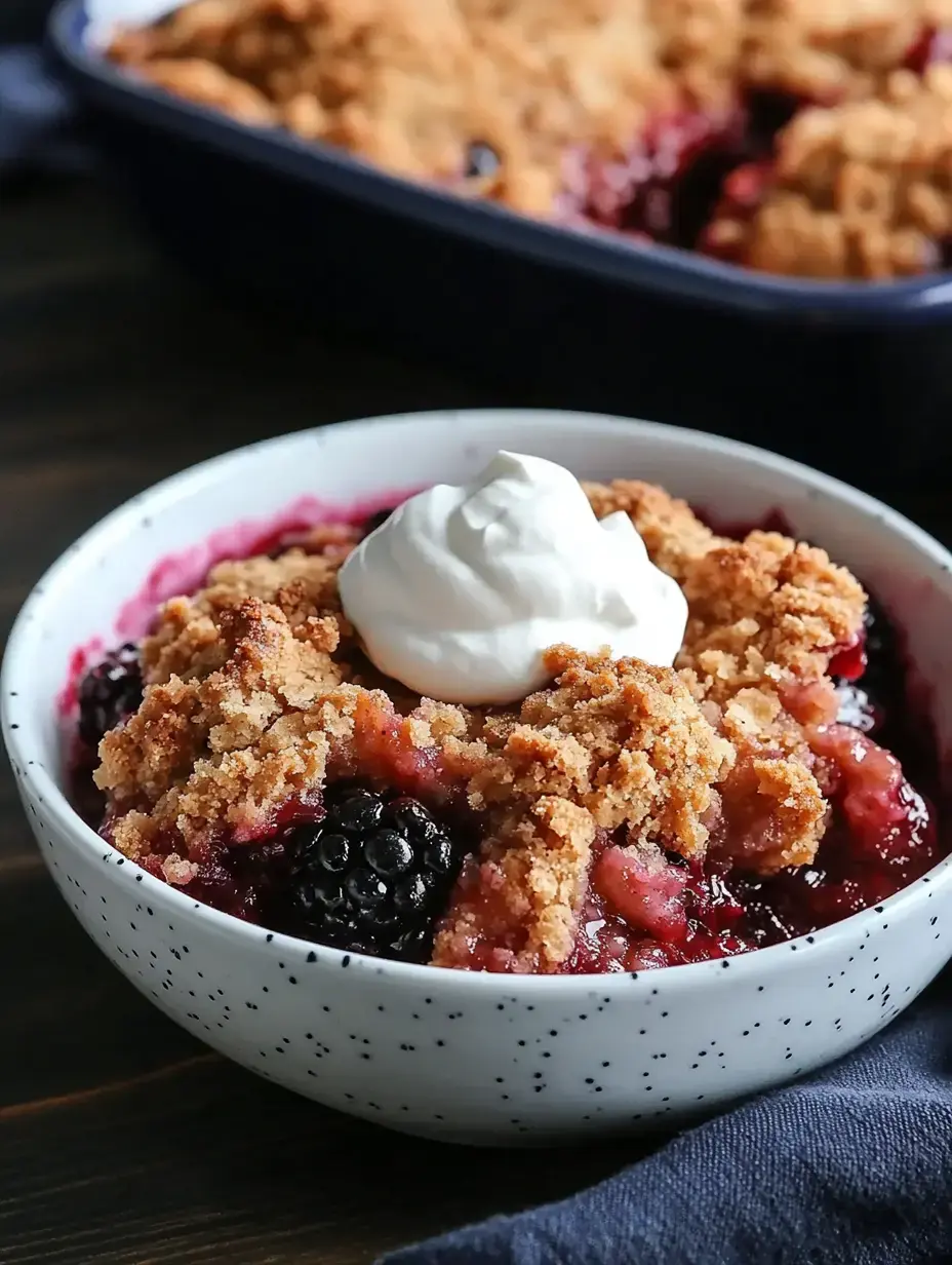 A bowl of berry crumble topped with a dollop of whipped cream sits on a wooden table.