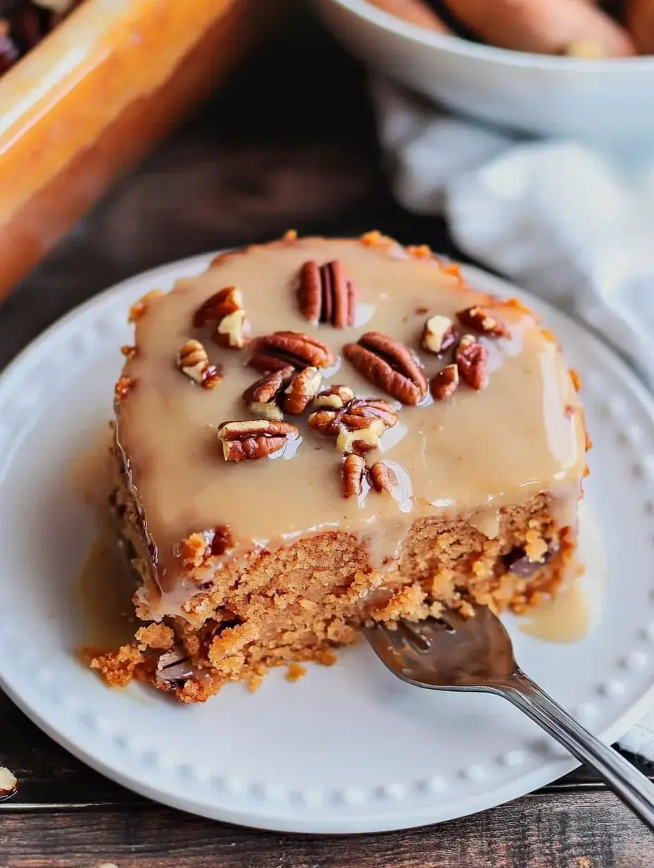 A slice of moist cake topped with a smooth, beige frosting and garnished with pecans, served on a white plate.