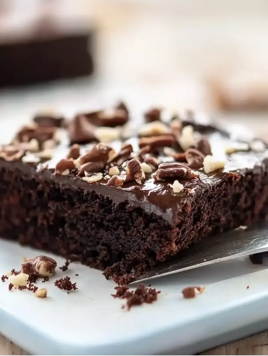 A close-up view of a chocolate brownie topped with nuts and a glossy chocolate glaze on a light blue plate.