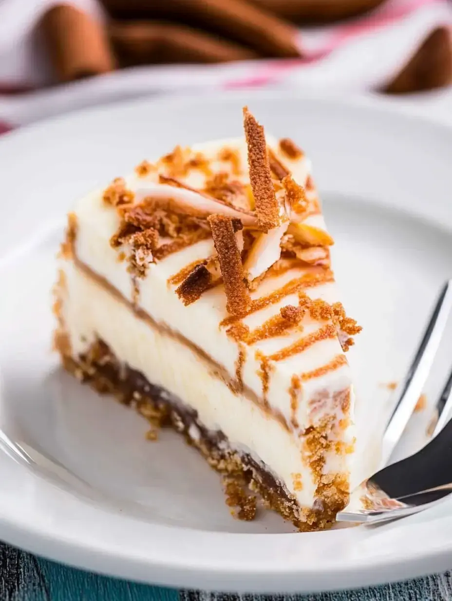 A slice of layered dessert features creamy filling, a chocolate layer, and a crumbly crust, topped with crispy pieces and drizzled lines.