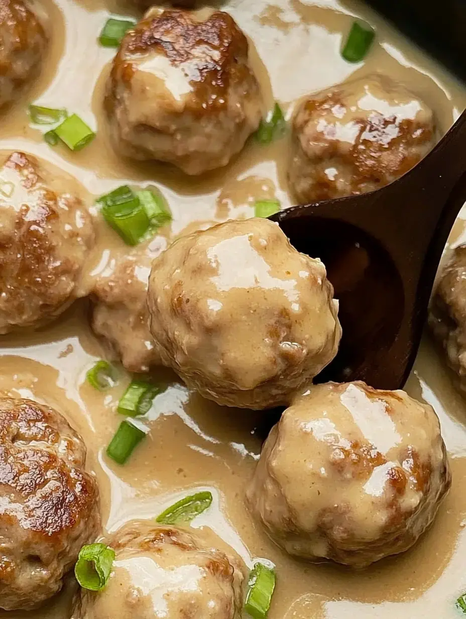 A close-up view of meatballs coated in a creamy sauce, garnished with chopped green onions.