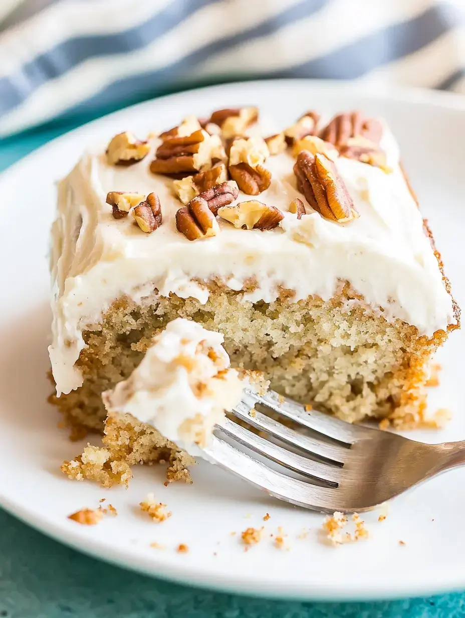 A slice of moist cake topped with cream cheese frosting and chopped pecans, with a fork delicately lifting a portion.