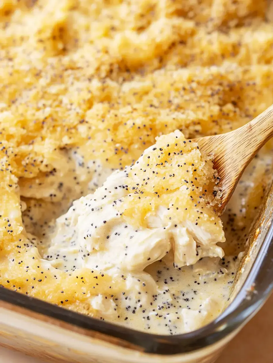 A close-up of a creamy casserole with a golden bread crumb topping and poppy seeds, being served with a wooden spoon.