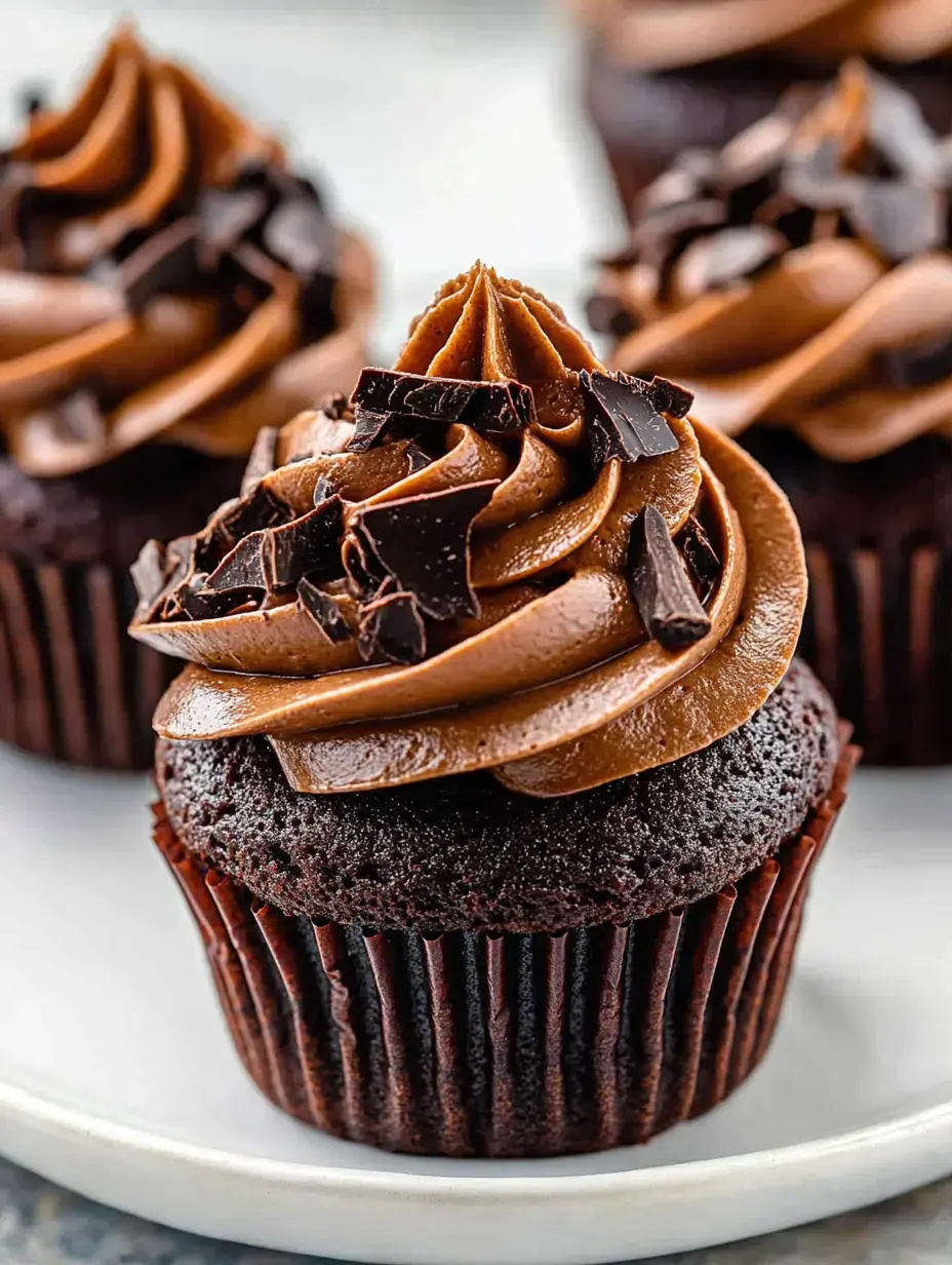 A close-up of a chocolate cupcake topped with swirls of chocolate frosting and chocolate shavings.