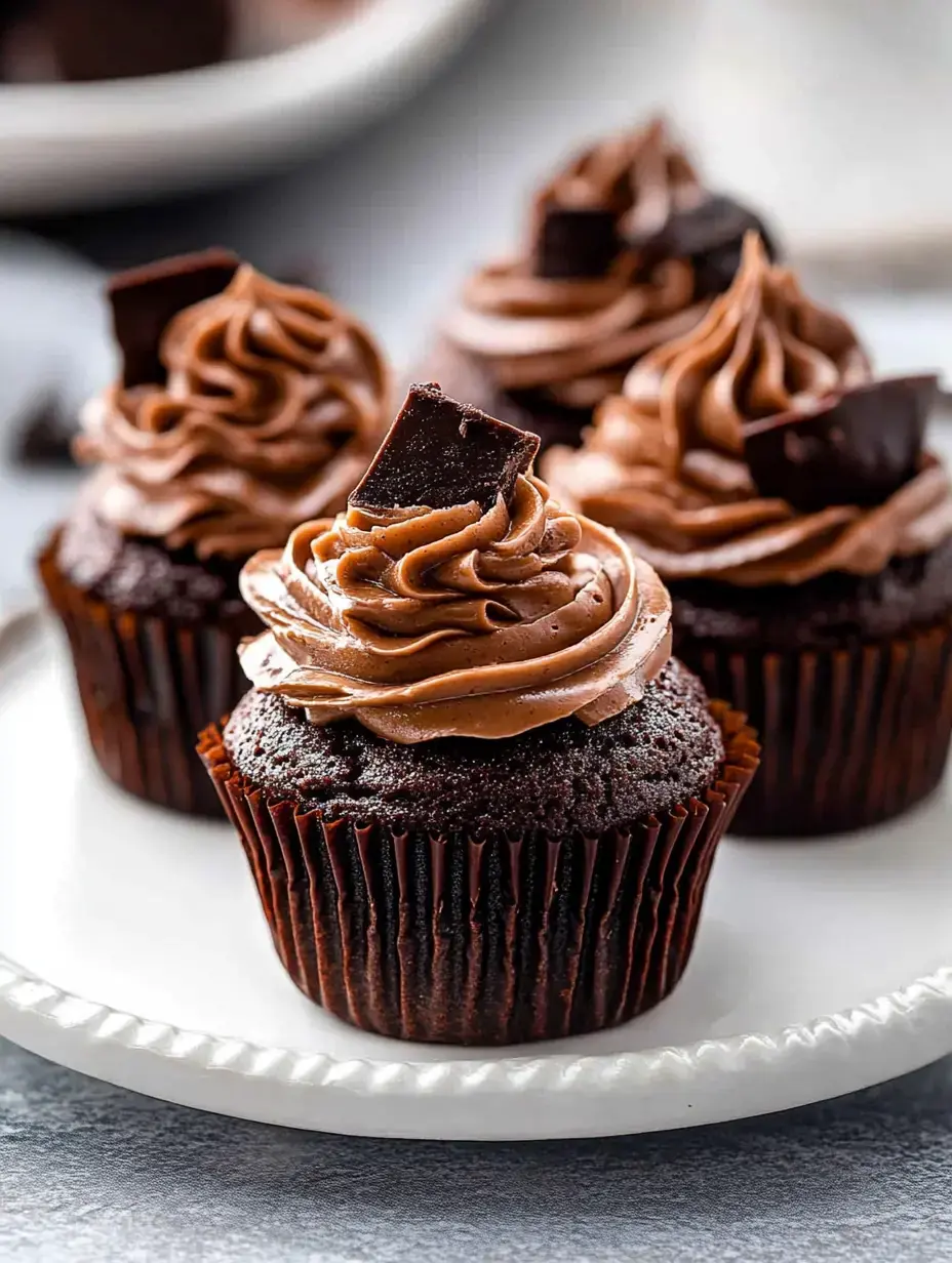 A plate of chocolate cupcakes topped with creamy chocolate frosting and a piece of chocolate on each.