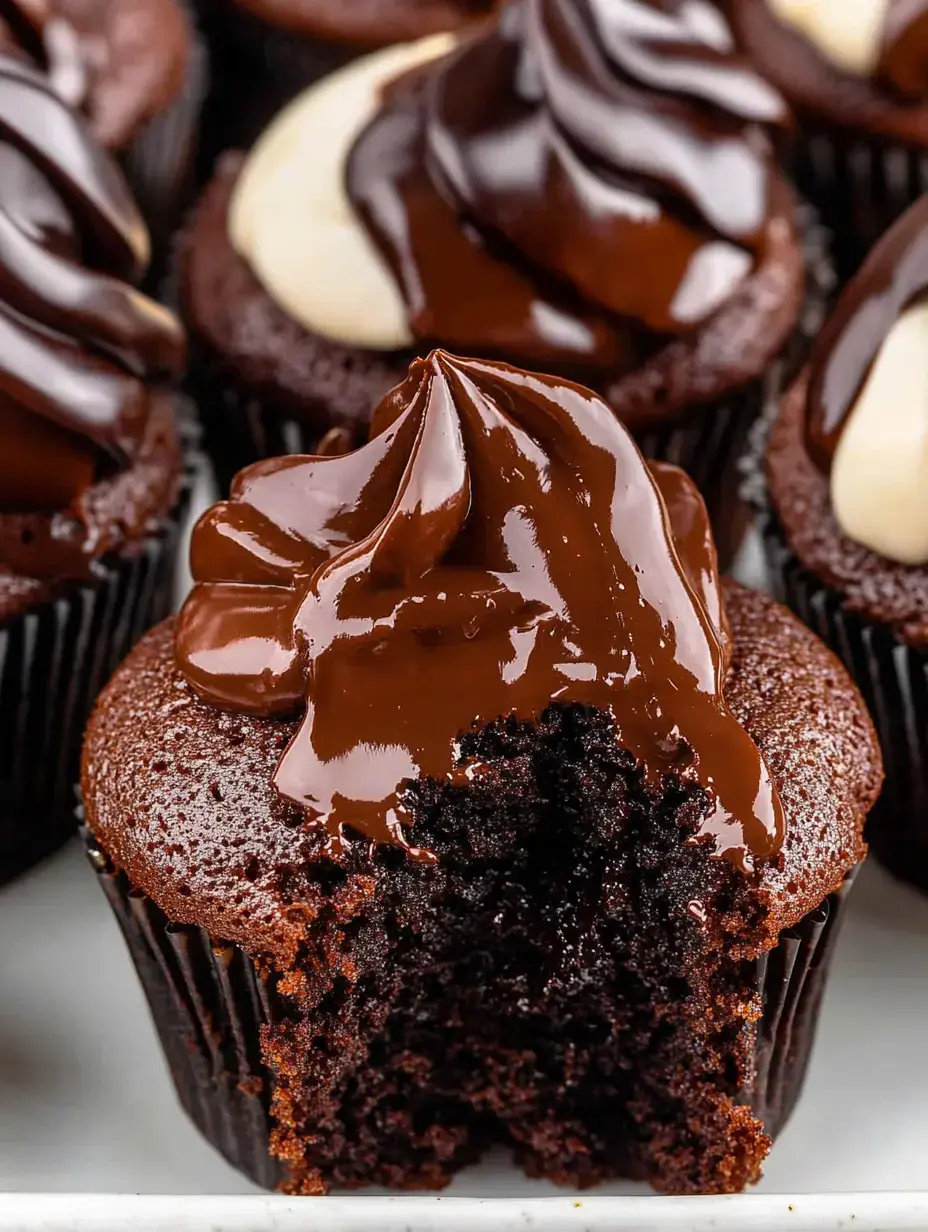 A close-up of a chocolate cupcake with a glossy chocolate frosting, featuring a bite taken out to reveal its moist interior.