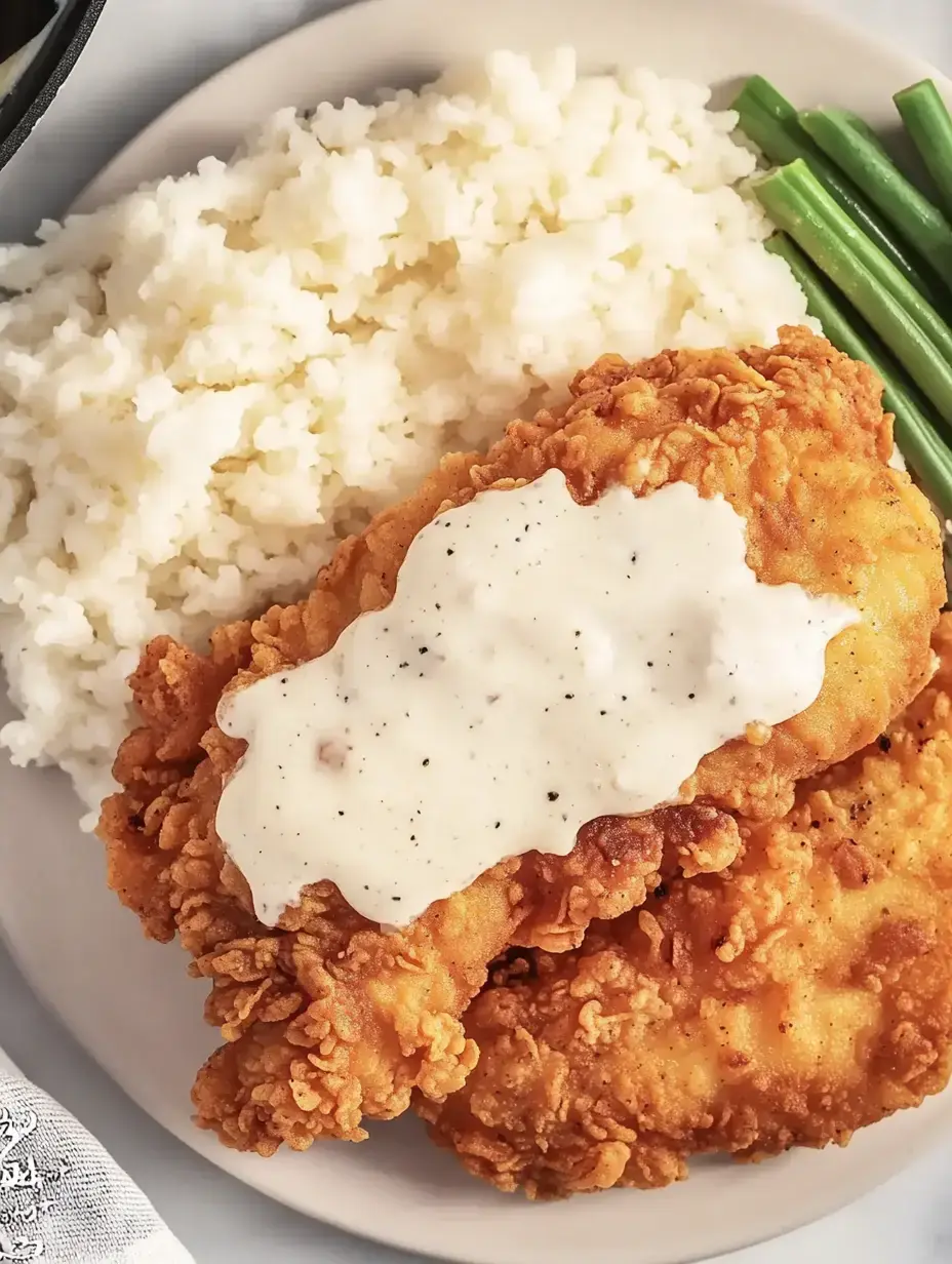 A plate of fried chicken topped with creamy gravy, served alongside mashed potatoes and green beans.